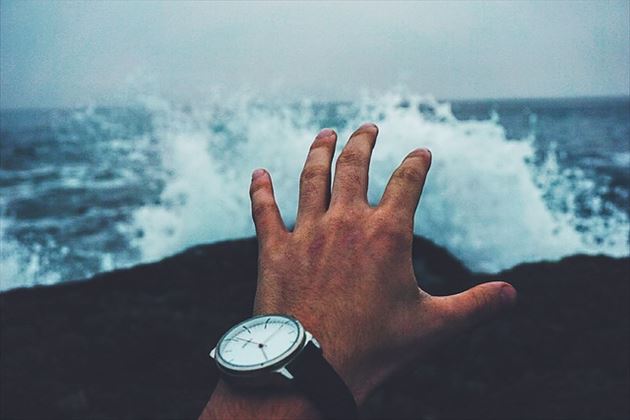 時計をした手と海